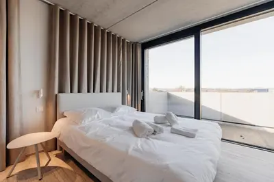 a bedroom with a white bed and a large window at Coliving - Bord de Meuse - L'instant in Oupeye