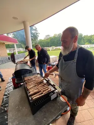 a man is cooking sausages on a grill at Camping San Lanaco in Lanaken