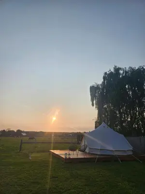 a tent in a field with the sunset in the background at Glamping met paarden in Nieuwerkerken