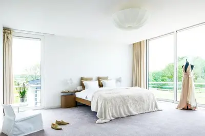 a white bedroom with a bed and a large window at Villa Bianca in Dalhem