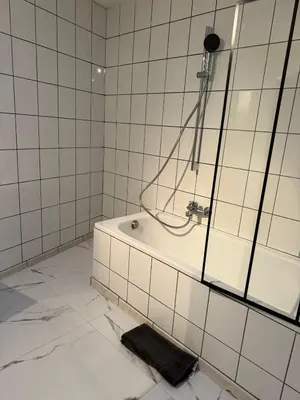 a white tiled bathroom with a tub and a shower at Studio Cosy rénové au Centre de Liège in Liège
