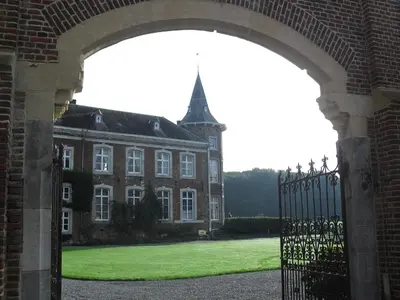 an open gate to a large brick building with a grass yard at Kasteel Nieuwenhoven in Sint-Truiden