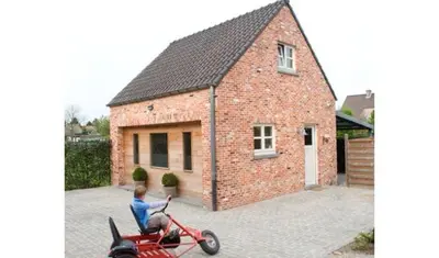 a man sitting on a motorcycle in front of a brick house at De Bosbeekpoort in Oudsbergen