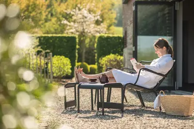 a woman sitting in a chair reading a book at côté verger B&B in Battice