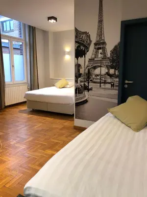 a bedroom with two beds and a picture of the eiffel tower at Hotel Le Cygne d'Argent in Liège