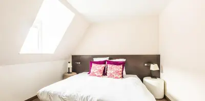 a bedroom with a white bed with pink pillows at Hotel Malpertuus in Riemst