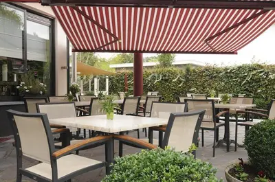 a patio with tables and chairs and a red umbrella at Hotel Limburgia in Kanne