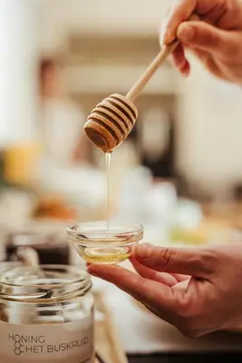 a person holding a wooden spoon pouring honey into a jar at Hotel Het Buskruid in Lummen