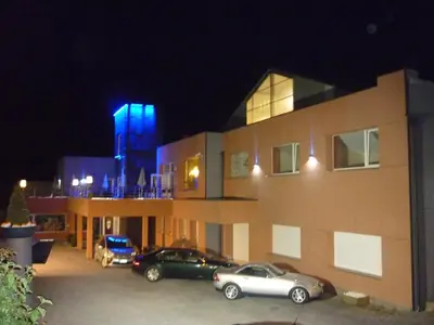 a building with cars parked in a parking lot at night at Hotel Le Midi in Petit-Rechain
