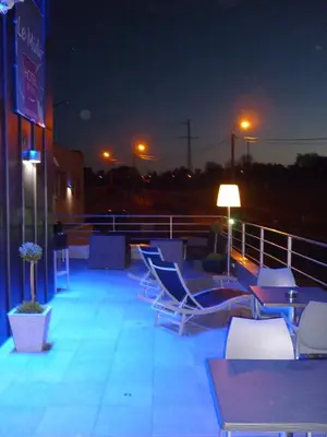 a group of chairs and tables on a deck at night at Hotel Le Midi in Petit-Rechain