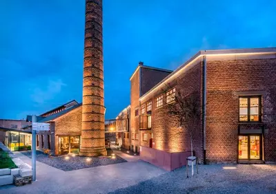 a brick building with a smoke stack next to a street at 't Poorthof in Borgloon
