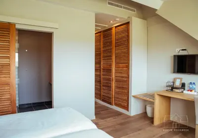 a bedroom with a bed and a kitchen with wooden shutters at Hoeve Roosbeek in Zepperen