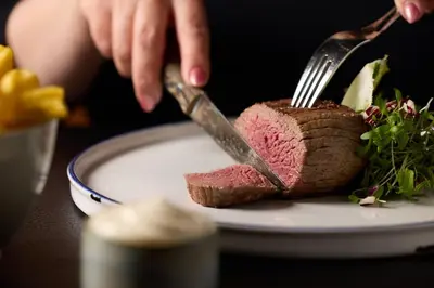 a person cutting a piece of meat on a plate with a fork at B&B Huize Briers in Bilzen