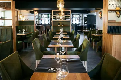 a restaurant with wooden tables and green chairs at La Couronne in Welkenraedt