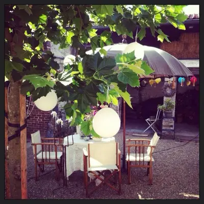 a table and chairs under an umbrella under a tree at B&B Domaine Villa Bayard in Kanne