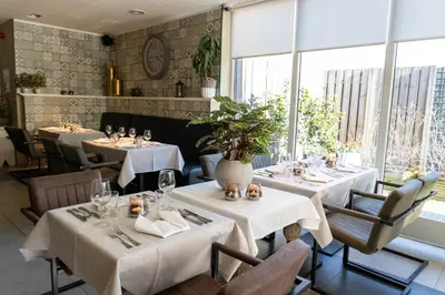 a restaurant with white tables and chairs and windows at Hotel De Maaskant in Maaseik