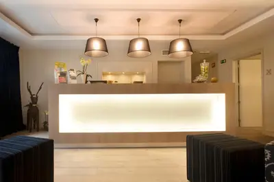 a lobby with a large white counter with three pendant lights at Tuinhotel in Lommel