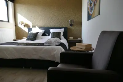 a bedroom with a large bed and a chair at Hotel Monte Cristo in Hoeselt