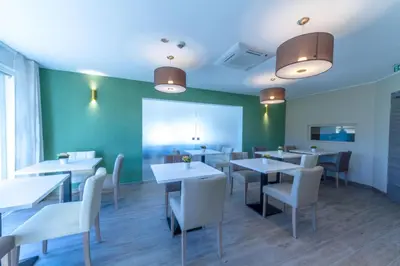 a restaurant with white tables and chairs and a green wall at ManavaHotel in Herstal