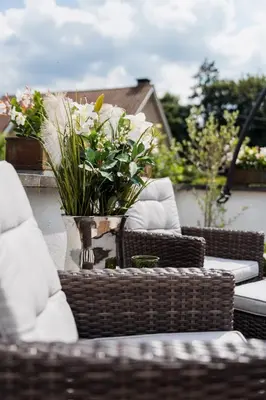 a table with wicker chairs and a vase with flowers at B&B Hof van Vervoering in Voeren