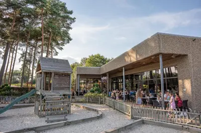 a group of people sitting outside of a building with a playground at Familiepark Goolderheide in Bocholt