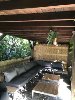 a patio with a black couch under a wooden roof at Vakantiehuis Elisa in Alken