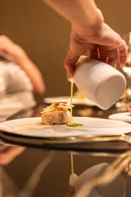 a person pouring food onto a plate on a table at Hotel De Barrier in Houthalen-Helchteren