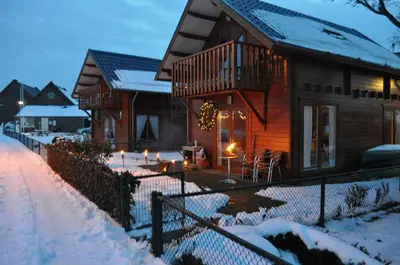 a wooden house with a deck in the snow at Thuiskomen, genieten aan het water in Maaseik