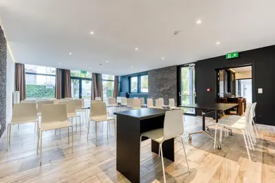 a dining room with white chairs and a black table at Hôtel Mosa in Hermalle-sous-Argenteau