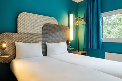 a bedroom with a large white bed with a blue wall at B&B HOTEL Liège Rocourt in Liège