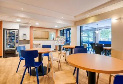 a room with tables and chairs and a kitchen at B&B HOTEL Liège Rocourt in Liège
