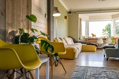 a living room with yellow chairs and a couch at ZussEnzo - STOER FAMILIEHUIS - 18P - 5SLPK - GROTE TUIN - SAUNA - OFYR BBQ - HOMECINEMA - 15MIN MAASTRICHT in Zussen