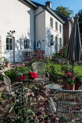 a patio with two chairs and an umbrella and flowers at PuurTeuven B&B tussen Kunst en Natuur in Voeren