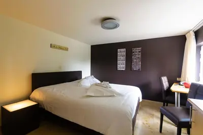 a bedroom with a white bed and a desk and a table at Hotel Pracha in Borgloon