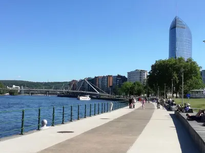 a sidewalk next to a river with people sitting on benches at Le Boisseliège in Liège
