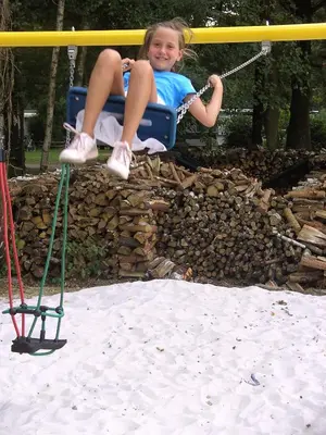 a little girl is sitting on a swing at Camping De Binnenvaart Superior Chalet in Houthalen-Helchteren