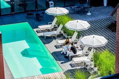 two people sitting in chairs under umbrellas next to a pool at Hof van Stayen in Sint-Truiden
