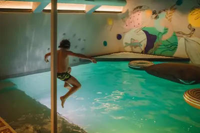 a boy jumping into a swimming pool in a room with a mural at Kindadom - Maison pour vacances insolites et inoubliables en Belgique in Montzen