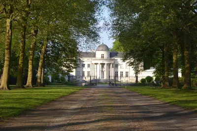 a large white house with a tree lined driveway at Kasteel Duras in Sint-Truiden