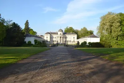 an empty road in front of a large white house at Kasteel Duras in Sint-Truiden