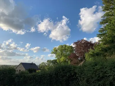 a blue sky with clouds and trees and a house at Gite de Caractère Le Lys Bleu in Limbourg