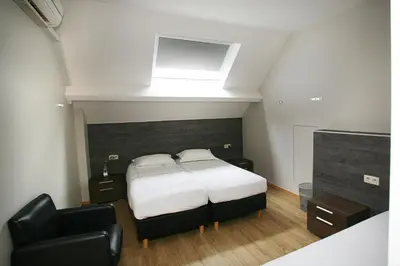 a bedroom with a bed and a black chair at Hotel Au Prince Royal in Leopoldsburg