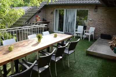 a patio with a wooden table and chairs on the grass at Vakantiewoning Het Wielje Maasland in Kinrooi