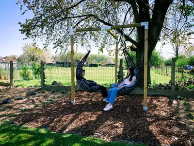 two people sitting on swings under a tree at Vakantiewoning Mèzik in Maasmechelen