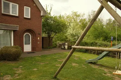 a swing set in a yard in front of a house at Holiday Home Op 't Busselen in Opoeteren