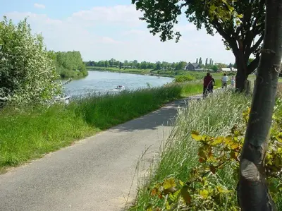 two people riding bikes down a road next to a river at Viva La Vie in Maaseik