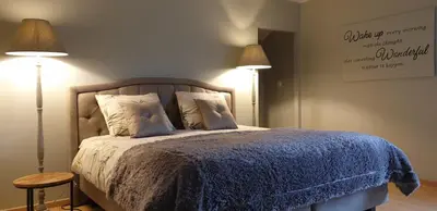 a bedroom with a bed with a blue blanket and two lamps at Prinsheerlyck in As