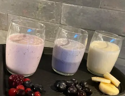 three glasses of milk and fruit on a table at B&B La Miniera in Genk