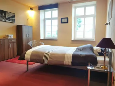 a bedroom with a bed with a table and two windows at Ferienwohnung in einem alten Bauernhaus in Lontzen