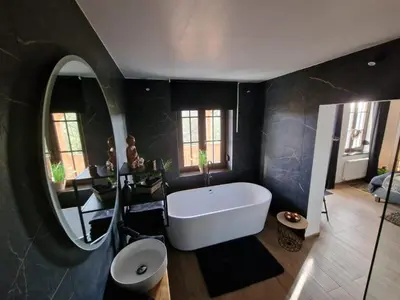 a bathroom with a white tub and a round mirror at Suite Tino in Verviers